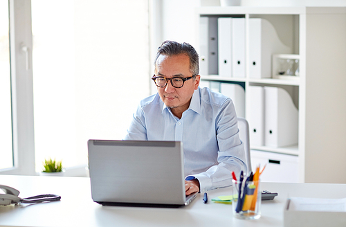 business, people and technology concept - businessman in eyeglasses with laptop computer office