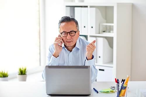 business, people, communication and technology concept - businessman with laptop computer calling on smartphone at office