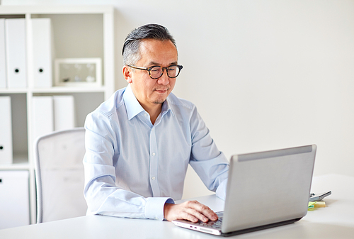 business, people and technology concept - businessman in eyeglasses with laptop computer office