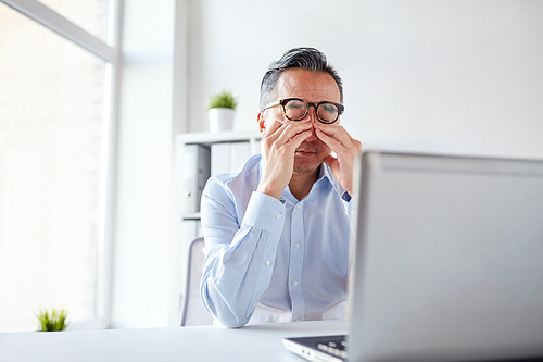 business, overwork, deadline and people concept - tired businessman in eyeglasses with laptop computer rubbing eyes at office