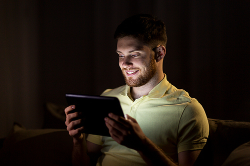 technology, internet, communication and people concept - happy smiling young man with tablet pc computer at night at home