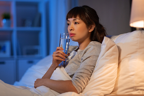 people, bedtime and thirst concept - asian woman drinking water at night in bed at home