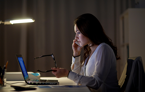 business, technology, overwork, deadline and people concept - woman with laptop calling on smartphone at night office