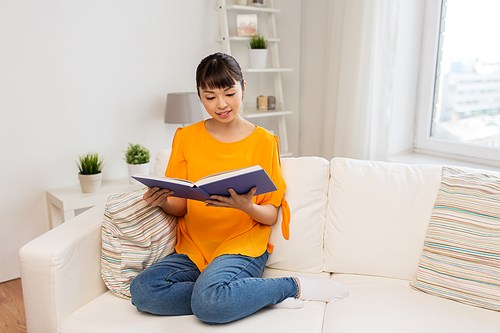 education, literature and people concept - smiling young asian woman reading book at home