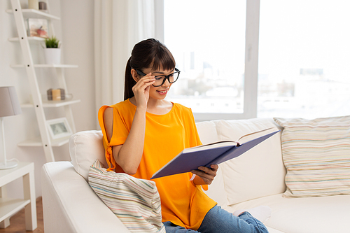 education, literature and people concept - smiling young asian woman in glasses reading book at home