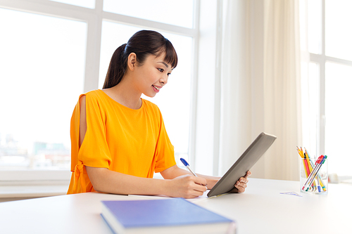 education, technology and people concept - happy smiling asian student girl with tablet pc computer learning at home