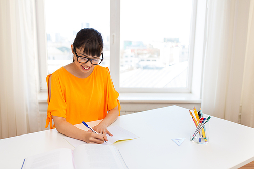 education, learning and people concept - happy asian student girl with book and notebook at home