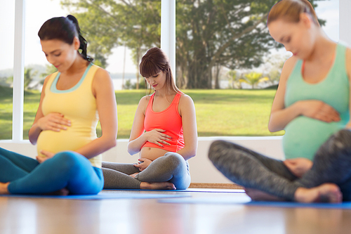 pregnancy, sport, fitness, people and healthy lifestyle concept - group of happy pregnant women exercising yoga in lotus pose in gym