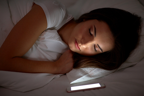 technology and people concept - young woman with smartphone sleeping in bed at home at night