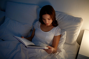 leisure and people concept - young woman reading book in bed at night home