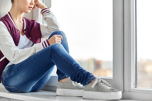 sadness and people concept - sad teenage girl sitting on window sill