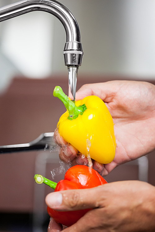 Kitchen porter washing red and yellow pepper under running tap