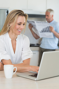 Smiling woman using laptop with partner standing with the paper