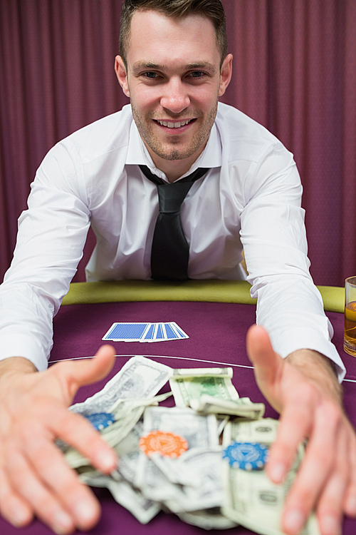 Happy man at poker table taking his winnings