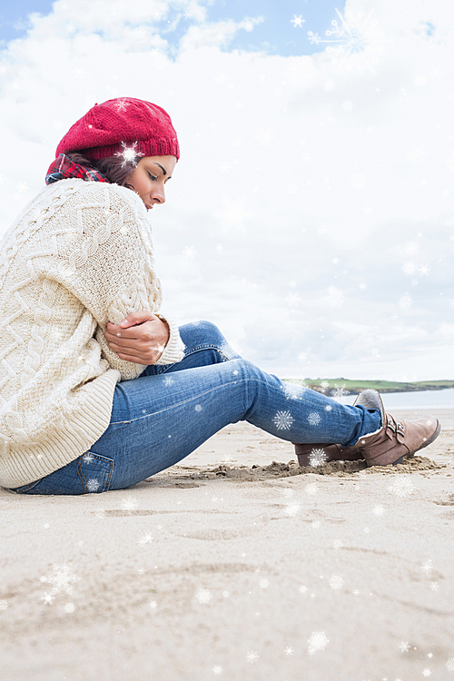 Composite image of woman in stylish warm clothing sitting at beach