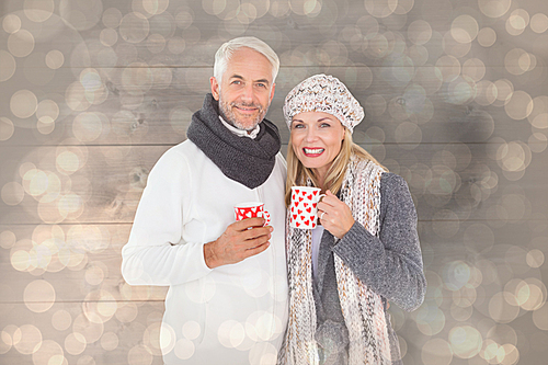 Composite image of happy couple in winter fashion holding mugs