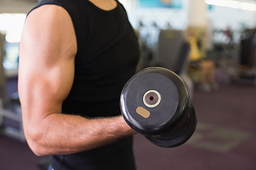 Mid section of man exercising with dumbbell in gym