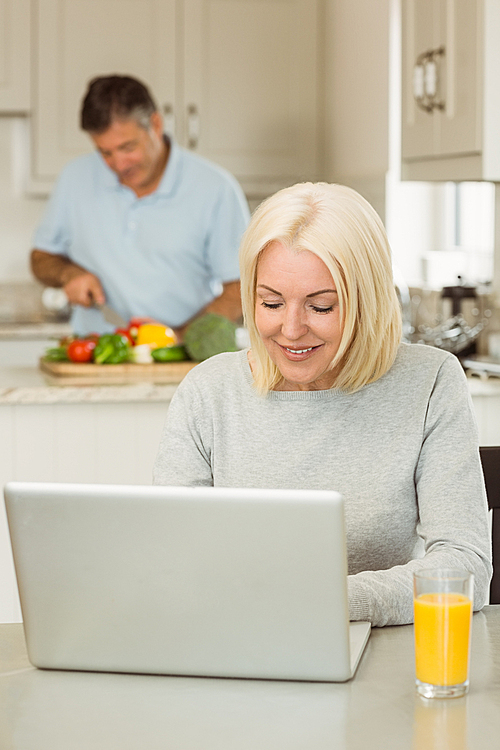 Happy mature blonde using laptop at home in the kitchen