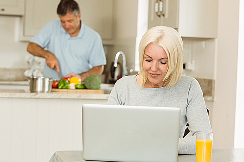 Happy mature blonde using laptop at home in the kitchen