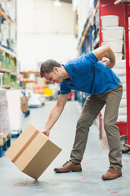 Side view of worker with backache while lifting box in the warehouse