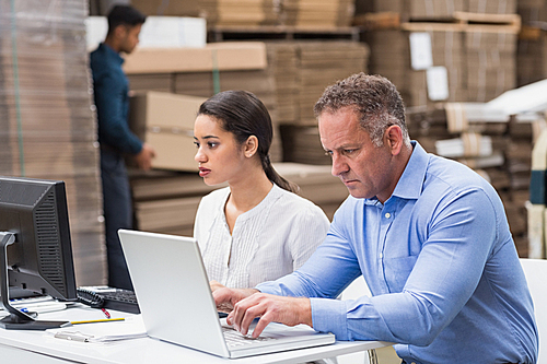 Warehouse managers working with laptop at desk in a large warehouse