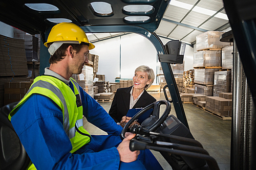 Warehouse manager talking with forklift driver in a large warehouse