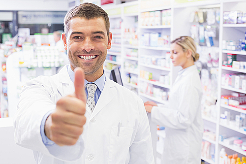 Happy pharmacist holding his thumb at pharmacy