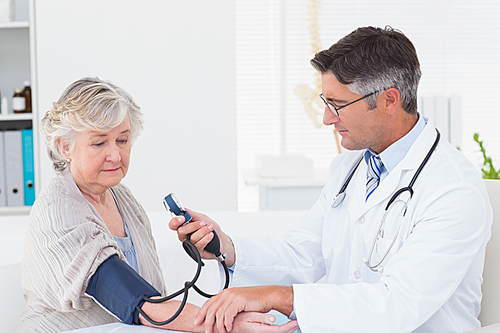 Male doctor checking female patients blood pressure in clinic