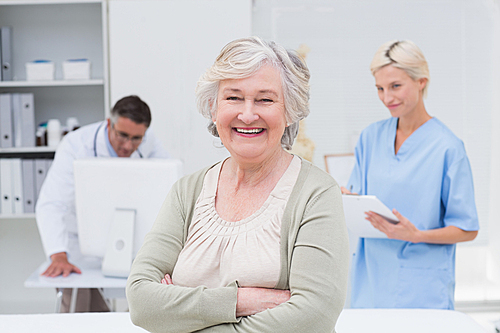 Portrait of senior patient smiling while doctor and nurse working in background at clinic