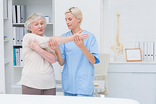 Nurse assisting senior female patient in raising arm at clinic