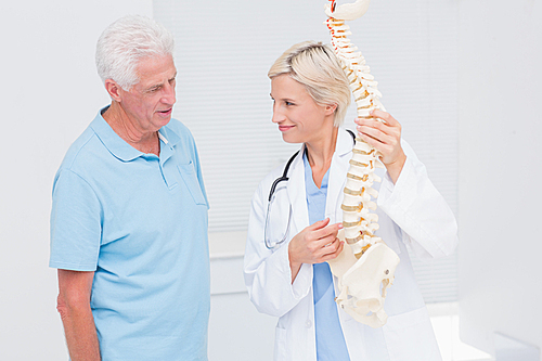 Female doctor and senior patient discussing over anatomical spine in clinic