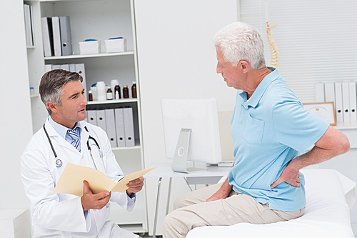 Male doctor discussing reports with senior patient suffering from backache in clinic