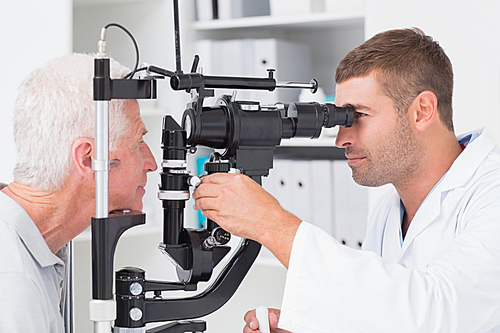 Male optometrist examining senior patients eyes through slit lamp in clinic