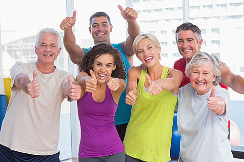 Portrait of happy friends gesturing thumbs up in fitness club