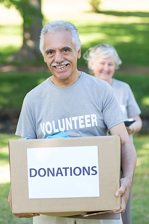 Happy volunteer senior holding donation box on a sunny day