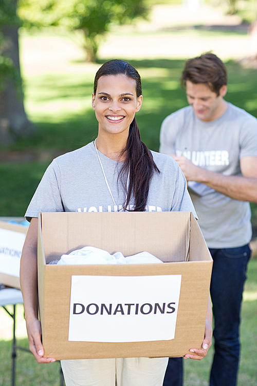 Happy volunteer brunette holding donation box on a sunny day