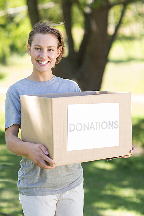 Happy volunteer in the park holding box on a sunny day