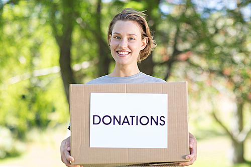 Happy volunteer in the park holding box on a sunny day