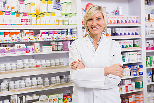 Blonde pharmacist with arms crossed smiling at camera in the pharmacy