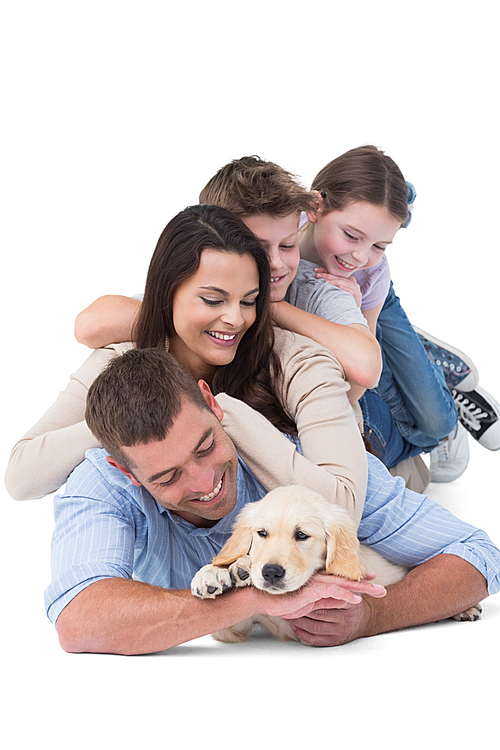 Happy family looking at puppy while lying on top of each other over white background