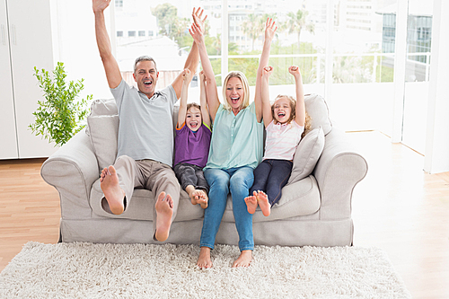 Happy family of four with arms raised sitting on sofa at home