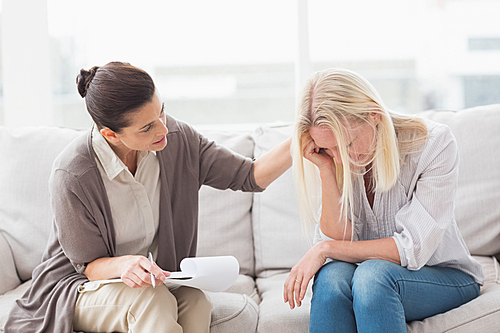 Therapist comforting upset woman on sofa in living room
