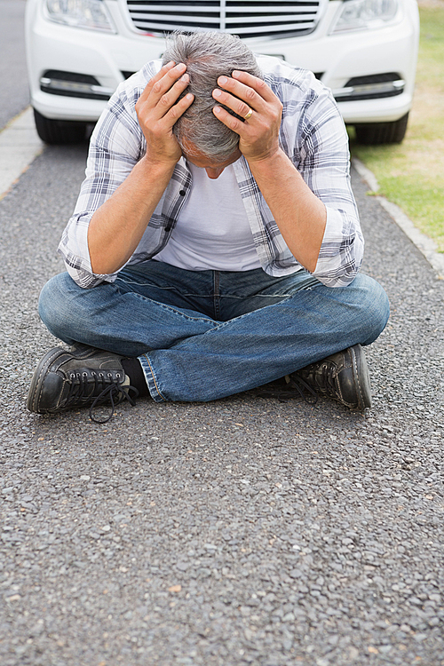 Stressed man sitting on the ground beside his car