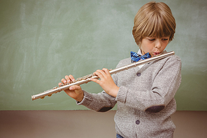 Portrait of cute little boy playing flute in classroom