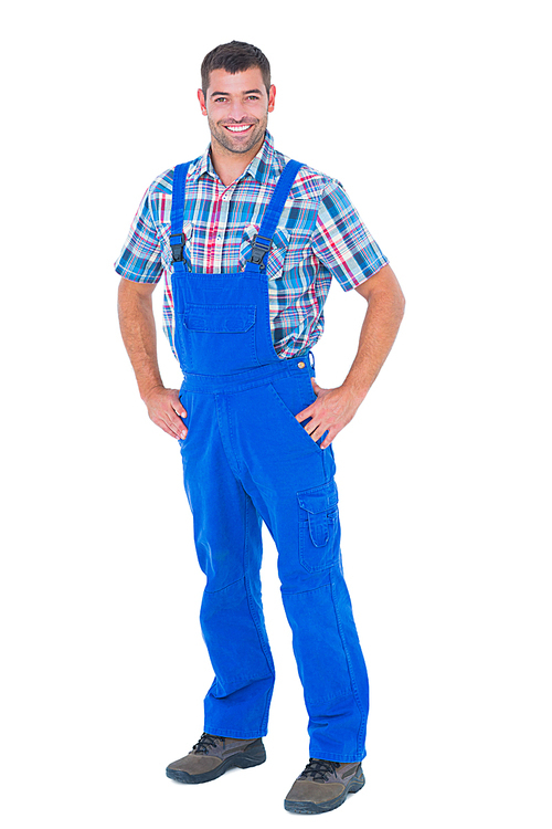 Full length portrait of happy handyman in coveralls standing hands on hip over white background