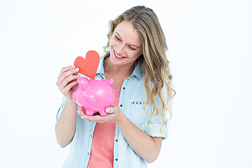 Smiling woman holding piggy bank and red heart on white background