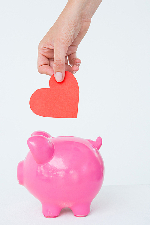 Woman holding piggy bank and red heart on white background