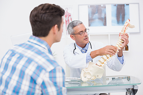 Doctor explaining anatomical spine to his patient in medical office