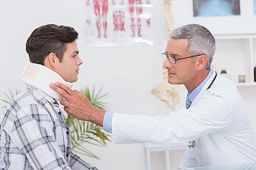 Doctor examining patient wearing neck brace in medical office