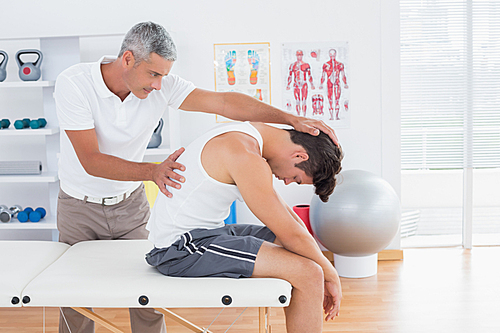 Doctor stretching a young man back in medical office